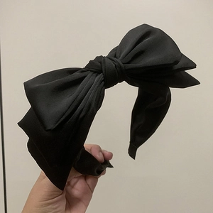 Close-up of a black fabric headband featuring a large triple-layered bow accessory