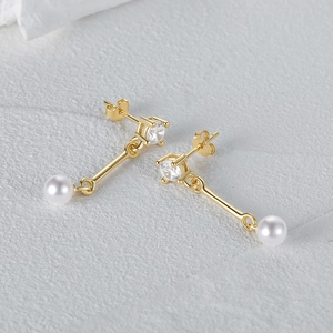 Detail of gold asymmetric earrings with sparkling zircons and elegant white pearls