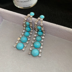 Gros plan de boucles d'oreilles bohèmes en turquoise et strass sur plateau en velours