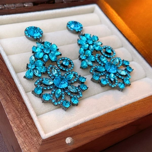 Vintage style blue rhinestone floral drop earrings displayed on a rustic jewelry box