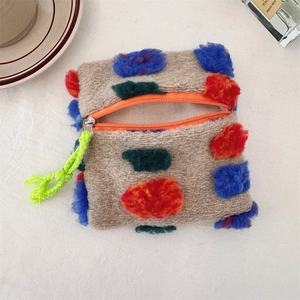 Detail view of plush brown cosmetic bag with colorful pom-poms and orange zipper