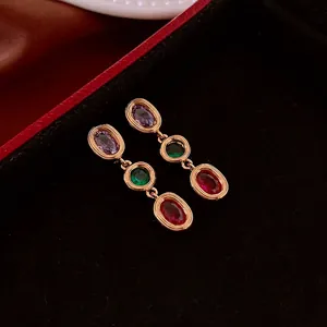 Vintage gold earrings with oval purple, green, and red gemstones on black velvet