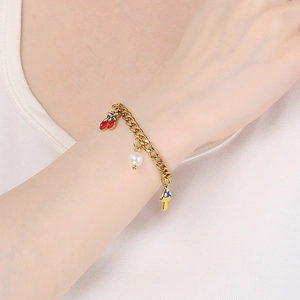 Détail d'un bracelet doré à gros maillons avec charms cerise, perle et champignon bleu