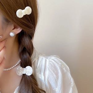 Detail of white resin bow hair clip and pearl jewelry set worn by a woman with braided hair
