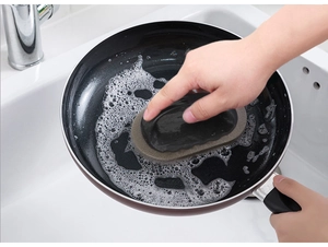 Detail showing a kitchen emery sponge brush cleaning a frying pan with an ergonomic handle