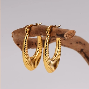 Chic gold-toned U-shaped earrings with spiral texture displayed on natural wood branch