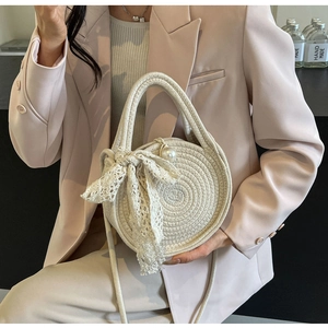 Detail of beige round woven crossbody bag with lace bow and large pearl charm accessory