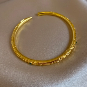 Vintage gold open bangle with embossed texture and green gemstones on champagne silk