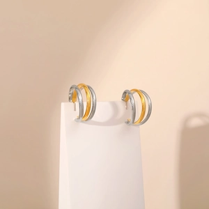 Macro shot of two-tone gold and silver twisted hoop earrings on white geometric stands