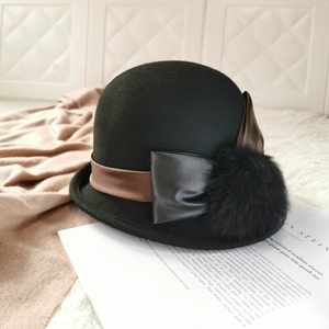 Close-up of black wool cloche hat with leather bow and fur pompom on beige blanket