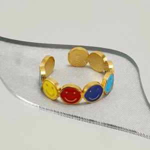 Bague ajustable en acier doré avec des smileys colorés en émail sur fond gris neutre