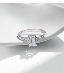 Macro shot of an emerald-cut clear gemstone ring with small side diamonds on a white base