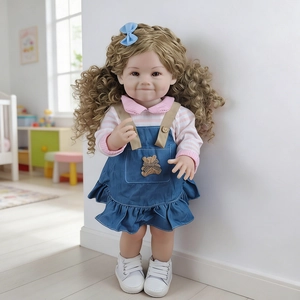 Detail of 55cm reborn baby doll with long blonde curls and denim dress in cozy setting