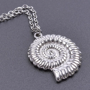 Macro shot of polished silver conch shell pendant featuring intricate spiral carvings and o-chain