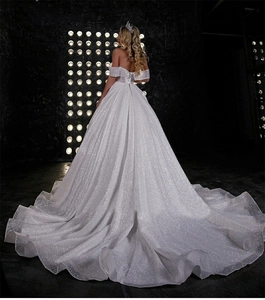 Detail of glittery fabric and long train on an off-shoulder sparkling wedding gown