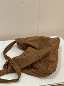 Detail of floral embroidery on a brown suede-like shoulder bag in a cozy indoor setting
