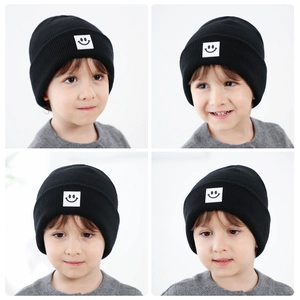 Dettaglio del cappello in maglia nera per bambini con toppa quadrata bianca sorridente