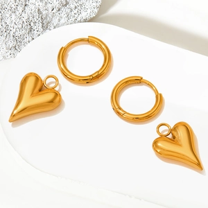 Polished gold heart drop earrings on a white minimalist pedestal with stone decor