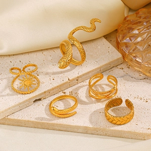Set of gold snake-shaped and textured stainless steel rings on beige stone and satin background