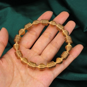Gold spiral spring coil bracelet with segmented ribbed design held over green silk