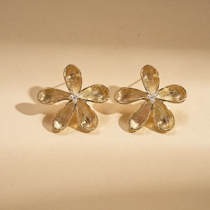 Macro detail of golden flower stud earrings with brushed texture and center beads