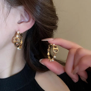 Detailed close-up of gold hoop earrings with white pearls and luxury logo on model