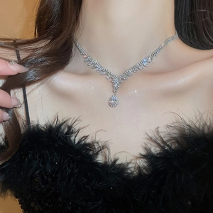Close-up of a silver V-shaped necklace with a sparkling pear-shaped drop pendant on model