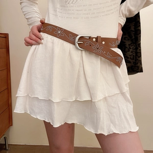Détail d'une ceinture en cuir marron avec rivets argentés et motifs floraux sur robe blanche