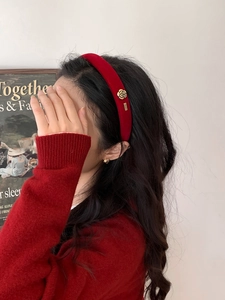 Detail view of red velvet headband featuring a golden camellia flower accent on a model