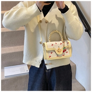 Detail of cream crossbody bag featuring red cherry print and twisted top handle