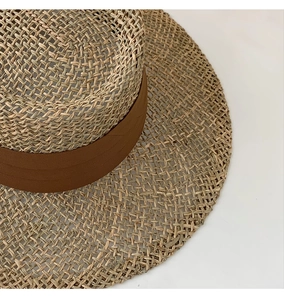 Close-up of natural woven seagrass straw hat featuring a brown ribbon trim detailing