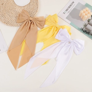 Satin bow hair clips in beige, yellow, and white displayed on a stylish flat lay