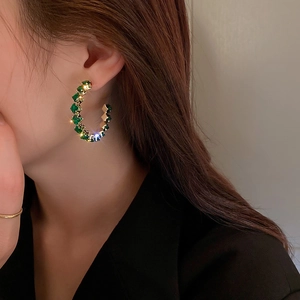 Detail of C-shaped gold earrings with square green crystals worn by a model