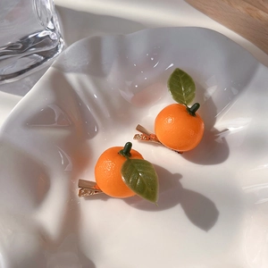Detail of realistic orange fruit hair clips with green leaves on a white ceramic plate