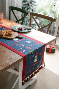 Close-up of blue Christmas table runner with snowman, reindeer patterns and red tassels
