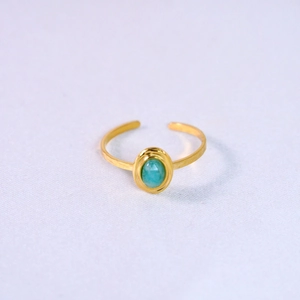 Detail of gold open ring with oval light blue gemstone on white fabric background