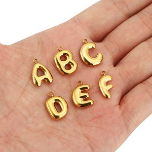 Gros plan de pendentifs lettres dorés bombés A-F dans une main pour bijoux DIY