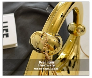 Detail of high-gloss gold metal handle with spherical accents and sleek snake chain strap