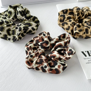 Three leopard print silk scrunchies in green, brown, and yellow colors on white background