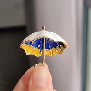 Close-up of golden umbrella brooch with blue enamel and sparkling star rhinestones
