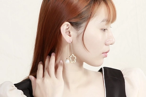 Close-up of asymmetrical golden clover earrings with pearl pendant on a model