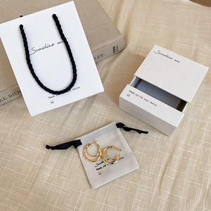 Detailed jewelry packaging set with gold earrings, white gift box and carry bag