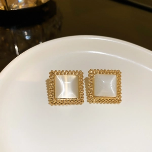 Detail of square gold-toned opal earrings with beaded edges on a white ceramic tray