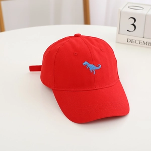 Détail de la casquette enfant en coton rouge avec broderie dinosaure bleu sur table blanche