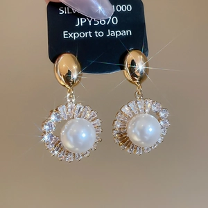 Macro detail of 18k gold plated silver earring with round pearl and sparkling rhinestones