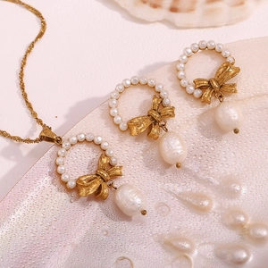 Detailed macro view of 18K gold bow pendant necklace with pearls on a wet surface