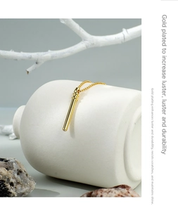 Detailed close-up of a gold-plated cylindrical pendant necklace on a ceramic decor