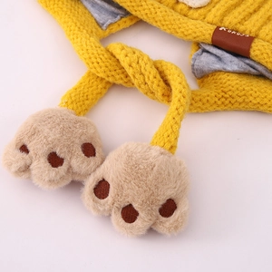 Detailaufnahme der gelben Baby-Strickmütze mit Plüsch-Pfoten und Lederetikett für den Winter