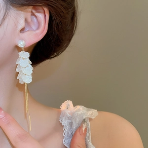 Detailed view of long white petal tassel earrings with gold chains worn by a female model