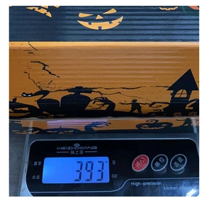 Detail shot of a Halloween pumpkin box being weighed showing its 393g total weight